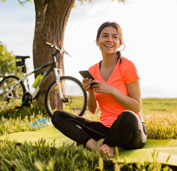 Een vrouw mediteert met gekruiste benen in een groen park, beoefent mindfulness en yoga in de buitenlucht om haar mentale gezondheid te verbeteren en stress te verlichten.