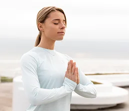 Een jonge vrouw beoefent meditatie met een rustige uitdrukking op haar gezicht, waarbij ze zich concentreert op mindfulness, ademhaling en geestelijke gezondheid.