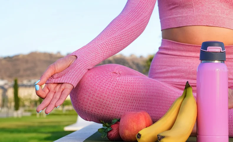 Vrouw die zich bij zonsopgang op een yogamat in de buitenlucht uitrekt met een fles water, ter promotie van een gezonde levensstijl en een ochtendroutine met fitness.